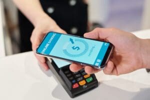 Hand of young man holding smartphone over terminal during contactless payment